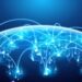 A digital illustration of a globe viewed from space, with illuminated lines and nodes connecting various points. The image represents global connectivity, the digital economy, and communication networks, with a blue and glowing visual aesthetic overlaid on a dark background. | COYYN