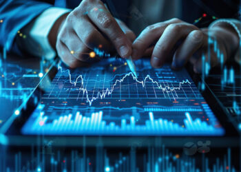 A person operates a tablet displaying financial charts and data. The screen shows a candlestick chart with peaks and troughs, set against a background of holographic graphs and financial icons, representing Coyyn Digital Finance and sophisticated stock market monitoring. | COYYN