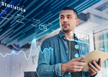 A man holds a tablet with a futuristic interface showing statistics from Coyyn.com Economy. The display includes a balance of $20,000, monthly income of $2,200, a savings rate of 50%, and trend lines. Months from January to April are visible, emphasizing the month of April and highlighting his economy management. | COYYN