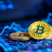 Three gold bitcoins rest on a digital screen displaying financial graphs and data in blue, hinting at cryptocurrency trading or market analysis—an intriguing landscape for freelancers exploring decentralized finance opportunities. | COYYN
