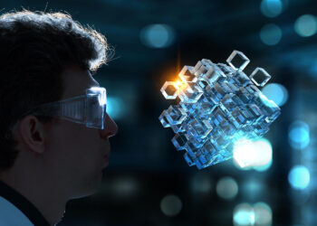 In a futuristic setting with blurred blue lights, a person wearing safety glasses examines a floating 3D holographic cube structure, symbolizing the intersection where AI meets blockchain, each smaller cube glowing with digital potential. | COYYN
