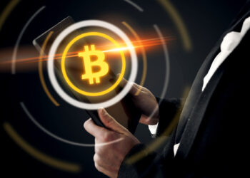 A person in a suit holds a tablet with a glowing Bitcoin symbol floating above it, surrounded by circular digital patterns. The background is dark, highlighting the gold Bitcoin logo and the orange light streak. | COYYN