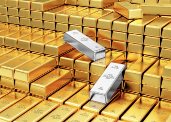 A large stack of shiny gold bars with two silver bars perched on top presents a striking contrast, inviting the question: Gold vs. Silver - Which Metal Is the Better choice? With gold's uniform gleam and silver's distinct shine, each metal tells its own story. | COYYN