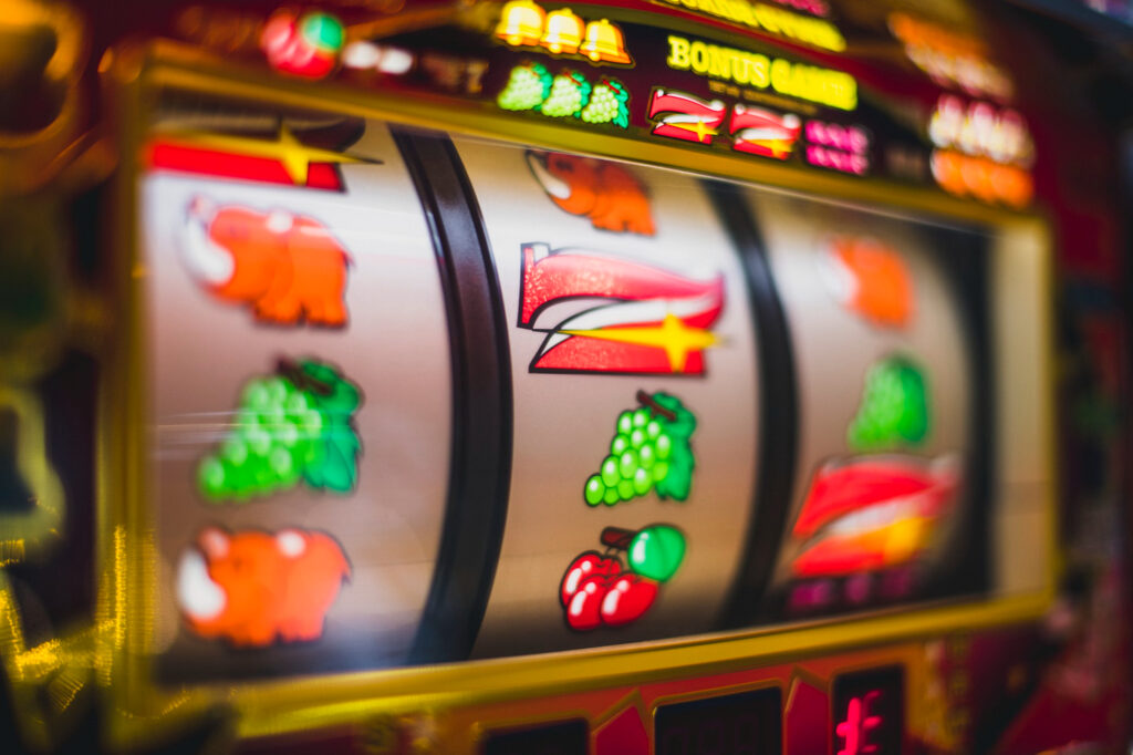 Close-up of a brightly lit slot machine at Bitcoin Casinos, with spinning reels displaying vibrant symbols like grapes, cherries, and a red number seven. The image is colorful and slightly blurred to convey motion. | COYYN