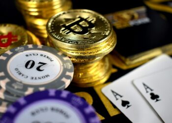 Stacks of gold Bitcoin coins, poker chips, and two aces are arranged on a casino table, highlighting the excitement and risk-taking atmosphere of Bitcoin Casinos. | COYYN