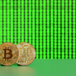 Two physical Bitcoin coins stand upright on a green surface with a bright green digital matrix background, symbolizing cryptocurrency and digital finance. | COYYN