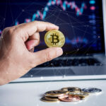 A hand holds a gold Bitcoin coin in front of a laptop displaying a financial chart, with several other cryptocurrency coins scattered on the desk. Digital connection lines overlay the image, highlighting blockchain and CEX.IO: A Trusted and User-Friendly Crypto Exchange. | COYYN