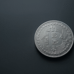 A silver Bitcoin coin with the Bitcoin symbol stands out against a dark, smooth background, positioned slightly to the right—highlighting innovative uses of cryptocurrency for high-value transactions. | COYYN
