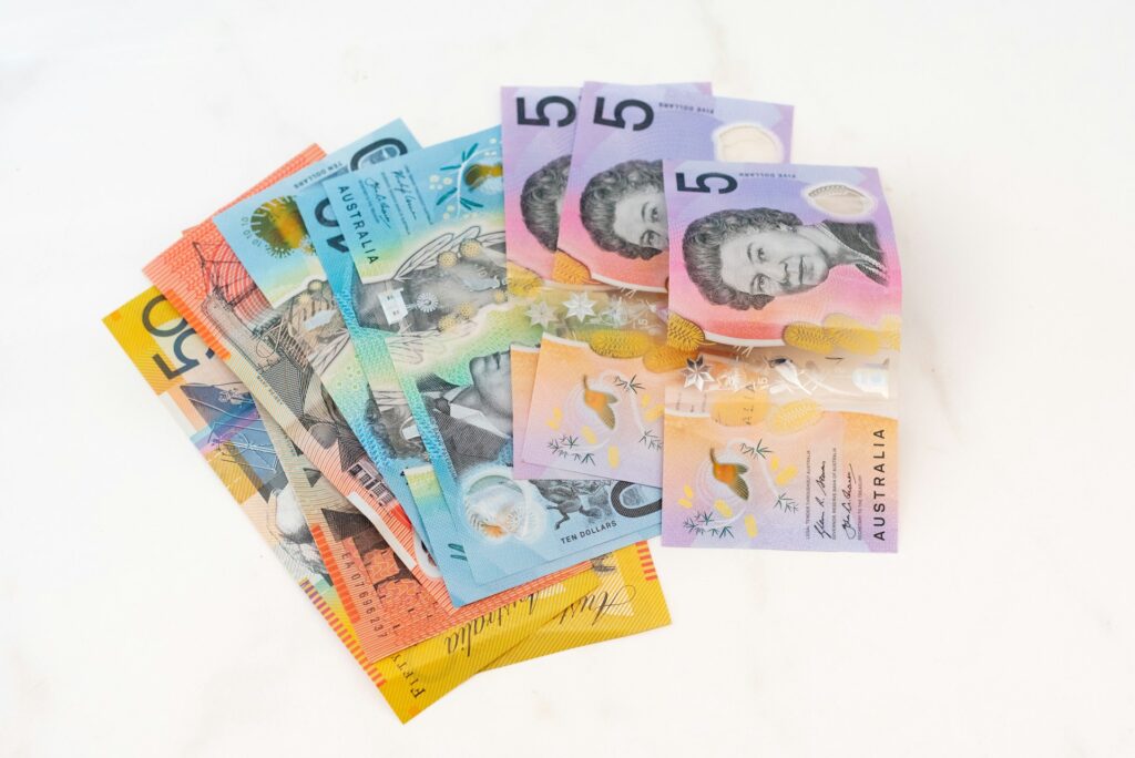 A pile of Australian dollar banknotes, including denominations of 5, 10, 20, and 50, displayed on a white surface—perfect for illustrating online business transactions in Australia. | COYYN