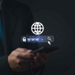 A person in a suit holding a smartphone, with a digital illustration of a globe and a web address bar featuring 'www', a search icon, and the word "Domain," symbolizing internet browsing or online search. | COYYN