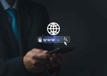 A person in a suit holding a smartphone, with a digital illustration of a globe and a web address bar featuring 'www', a search icon, and the word "Domain," symbolizing internet browsing or online search. | COYYN