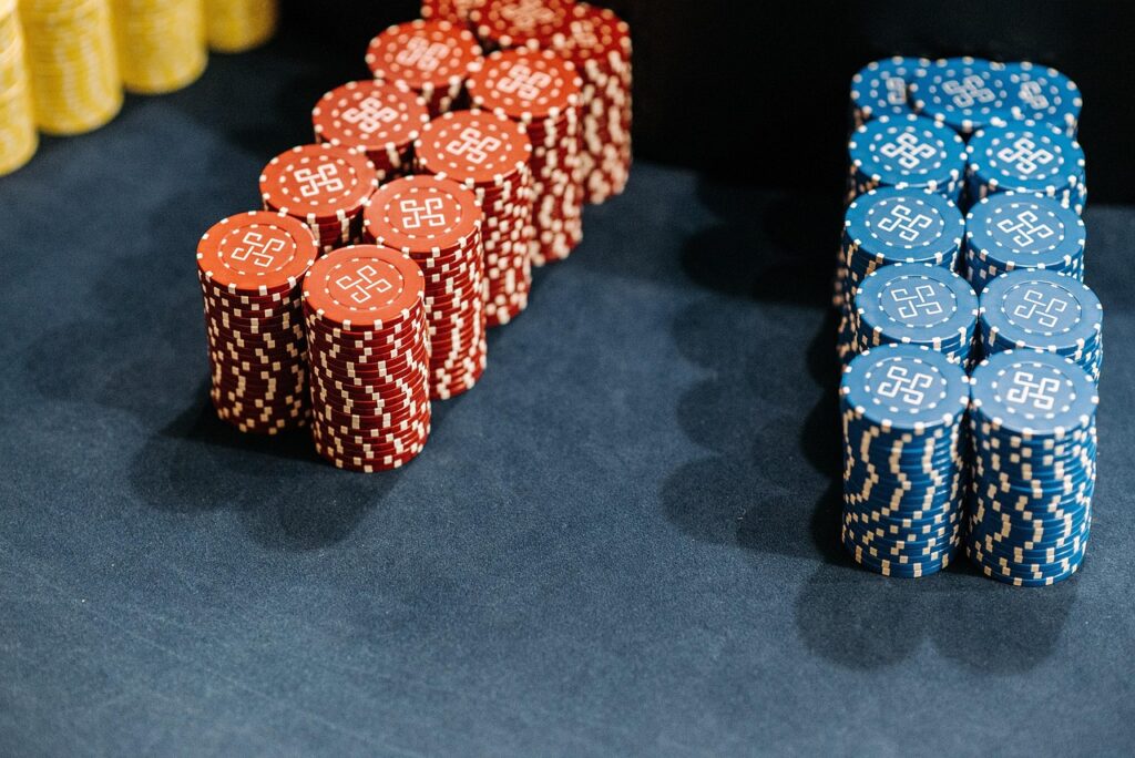 Stacks of red and blue poker chips are neatly arranged on a dark surface, evoking the thrill of an online casino, with yellow chips partially visible in the background. Each chip features a distinctive white pattern on top. | COYYN