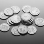 A scattered pile of various silver bullion coins featuring different designs—animals, people, and symbols—rests on a smooth grey surface. | COYYN