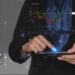 A person in a suit uses a tablet displaying a digital stock trading chart and financial data.