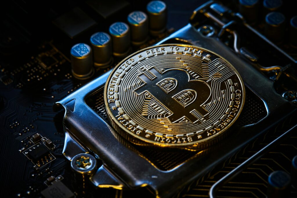 A gold physical Bitcoin coin rests on a computer motherboard, highlighting the digital currency's connection to technology and electronic transactions. | COYYN