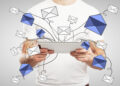 A person in a white shirt holds a tablet, with illustrated blue and white envelopes appearing to fly out from the screen, symbolizing sending or receiving emails. | COYYN