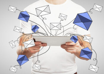 A person in a white shirt holds a tablet, with illustrated blue and white envelopes appearing to fly out from the screen, symbolizing sending or receiving emails. | COYYN