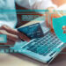 A person holding a credit card while using a laptop, with digital security icons and graphics overlaid, representing online payment and cybersecurity. | COYYN