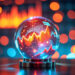 A glass sphere displays glowing financial graphs and charts, with red and yellow trend lines, against a blurred background of blue and orange lights, suggesting financial forecasting or data analysis. | COYYN