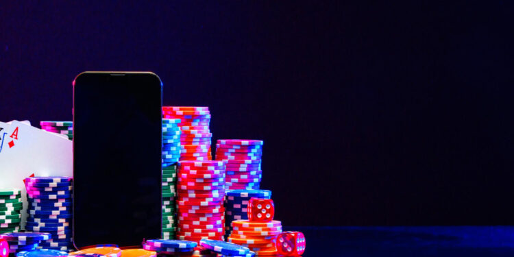 A smartphone stands among colorful poker chips, playing cards, and dice on a reflective surface, with a dark background, suggesting an online casino or gambling theme. | COYYN