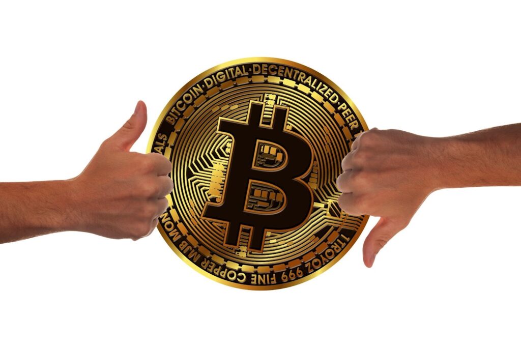 A large gold Bitcoin coin is shown in the center, with a hand on the left giving a thumbs up and a hand on the right giving a thumbs down, all against a white background. | COYYN